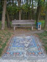 Mosaik bei einer Holzbank im Landschaftspark Herzberge in Berlin-Lichtenberg
